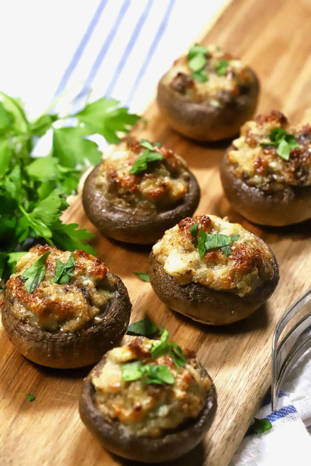 Six baked stuffed mushrooms on a cutting board. 