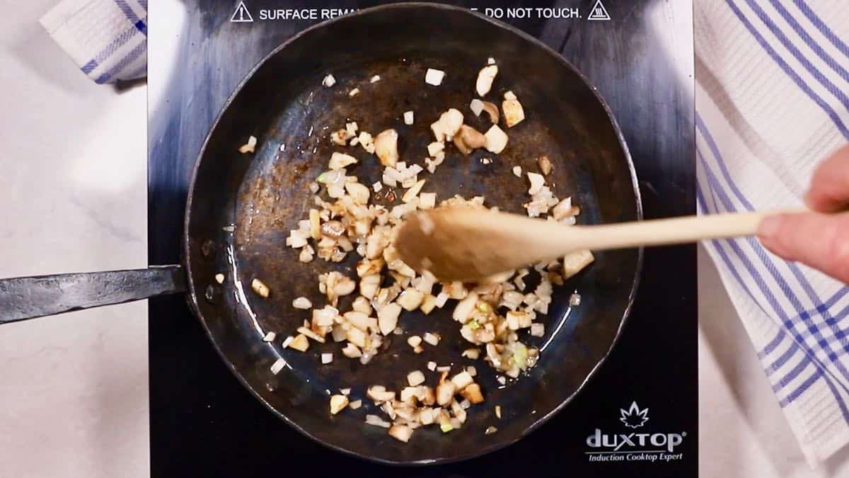 Chopped artichokes and shallots cooking in a skillet. 