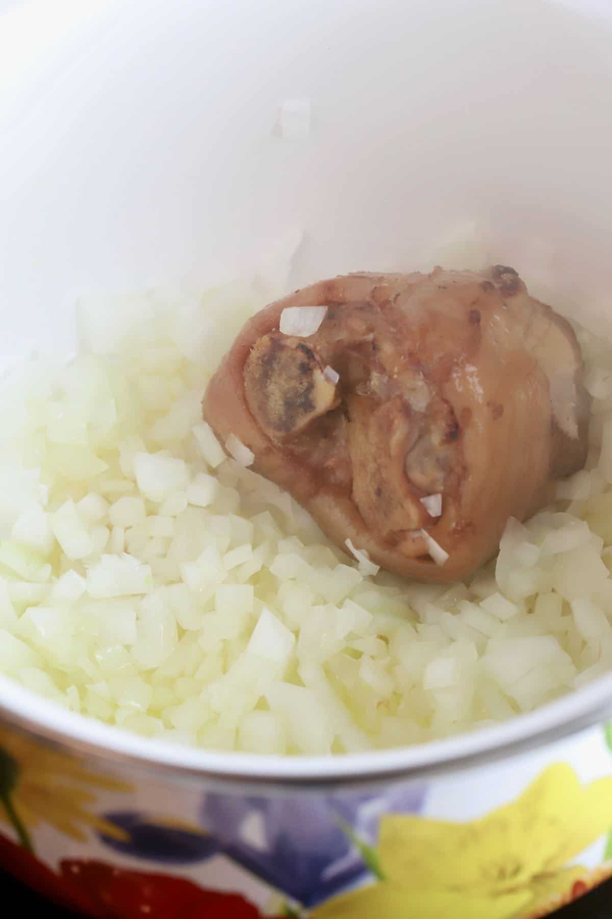 Cooking onions and a ham hock in a saucepan.