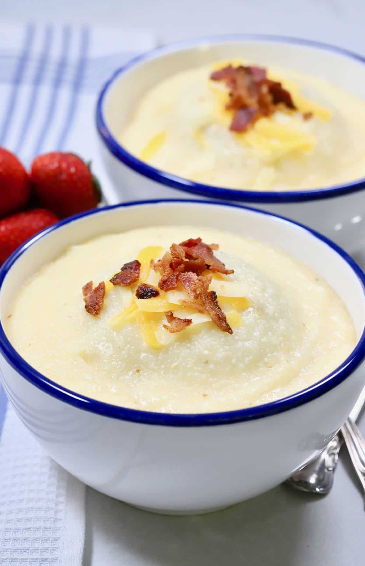 Two bowls of cheese grits topped with bacon. 