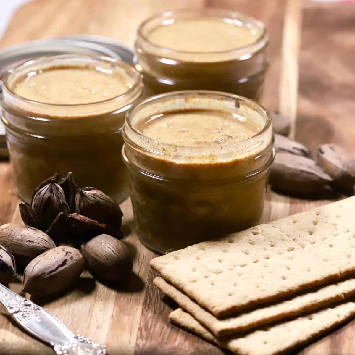 Homemade pecan butter in three glass jars with graham crackers.