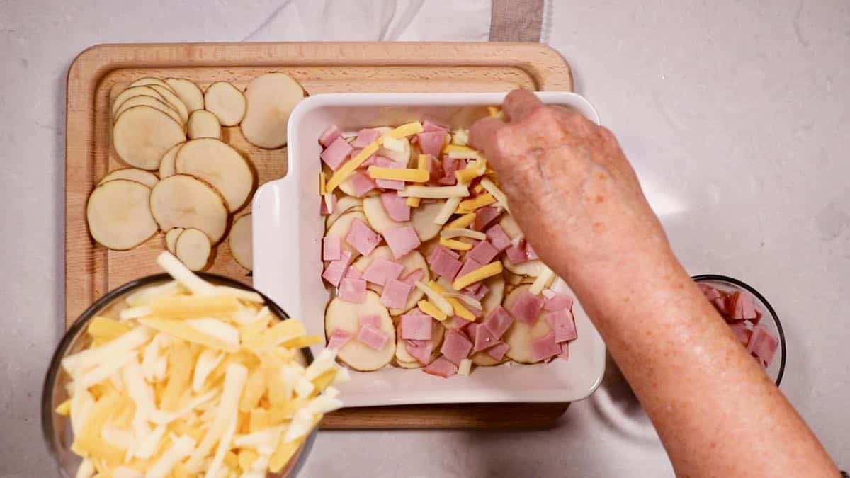 A baking dish with a layer of sliced potatoes, ham and cheese. 
