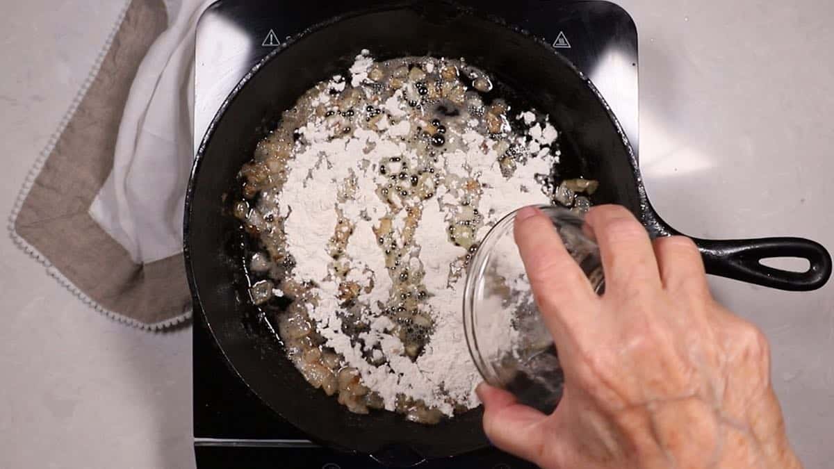 Adding flour to cooked onions in a skillet. 