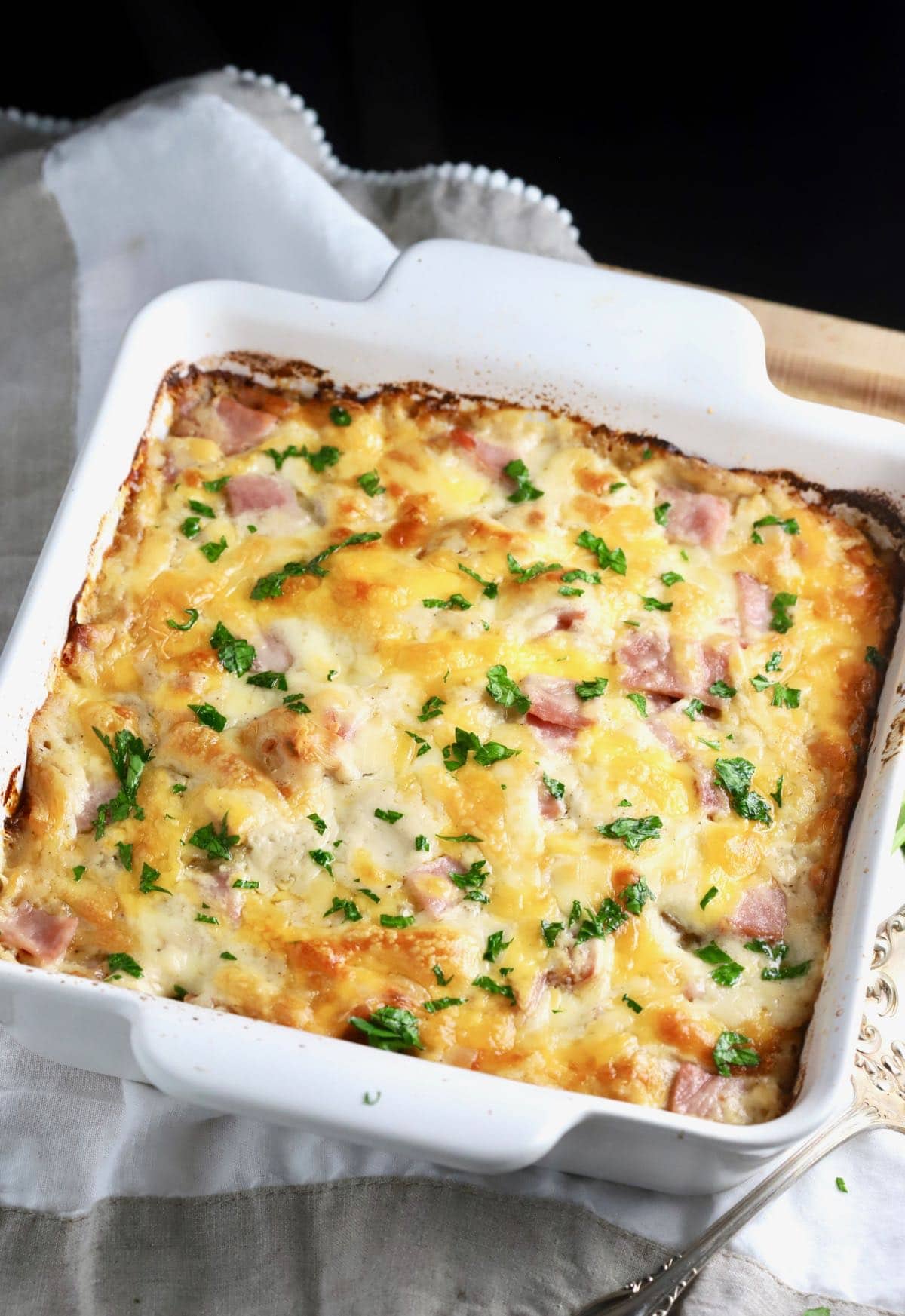 Au gratin potatoes and ham cooked in a white baking dish. 