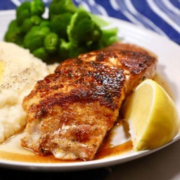 A blackened grouper filet on a plate with grits, garnished with a lemon slice.