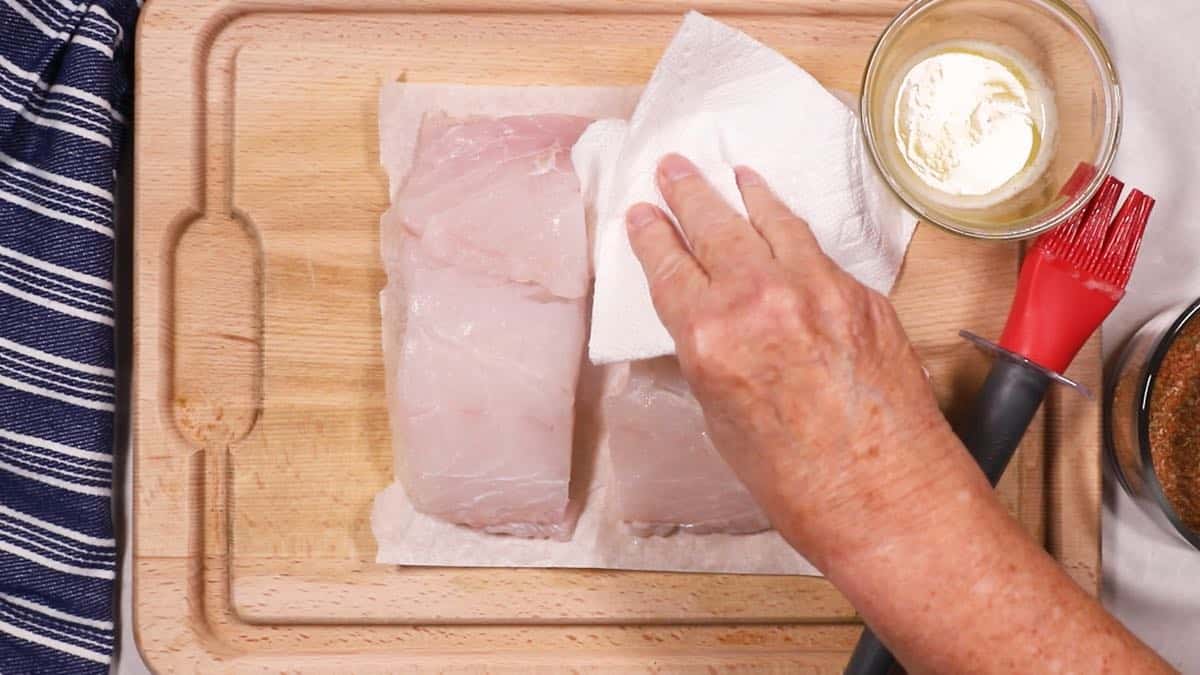 Using a paper towel to dry fish fillets. 