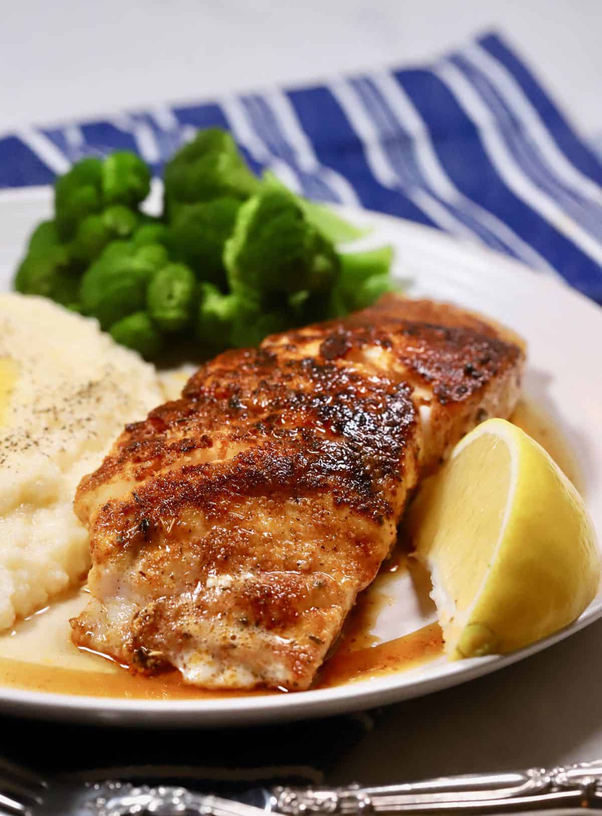 Blackened grouper on a white plate with grits.