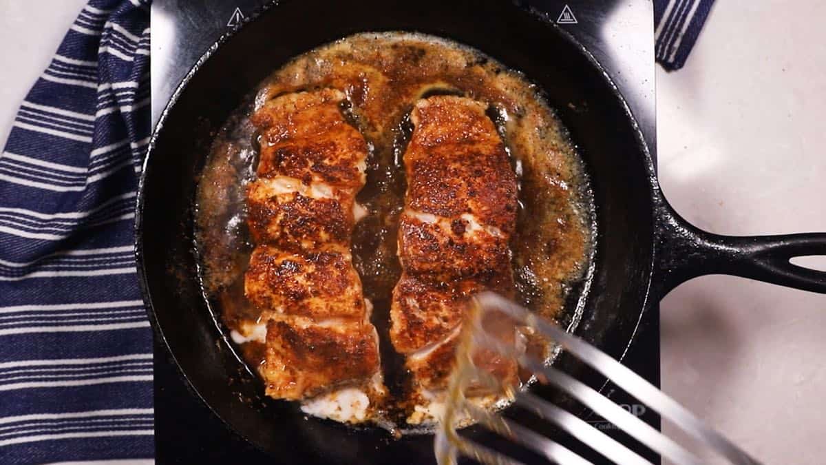 Two grouper fillets cooking in a cast-iron skillet. 