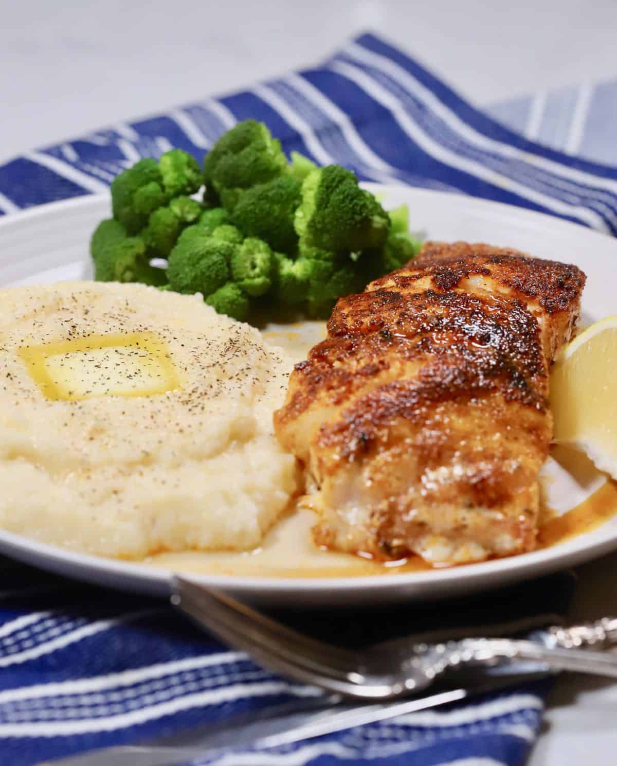 Blackened grouper fillet with grits and broccoli on a plate. 