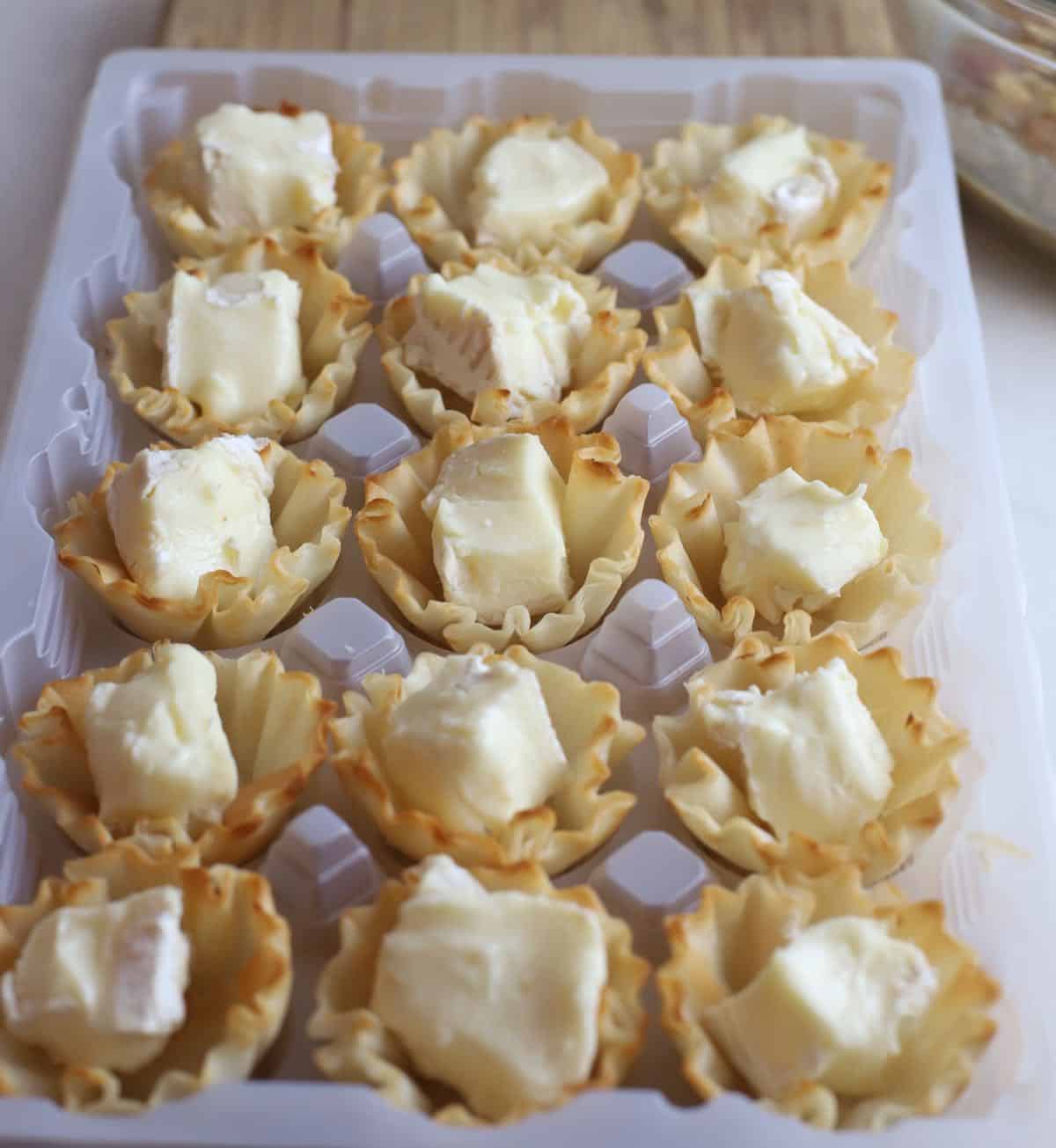 Cubes of brie cheese in phyllo shells on a baking sheet. 