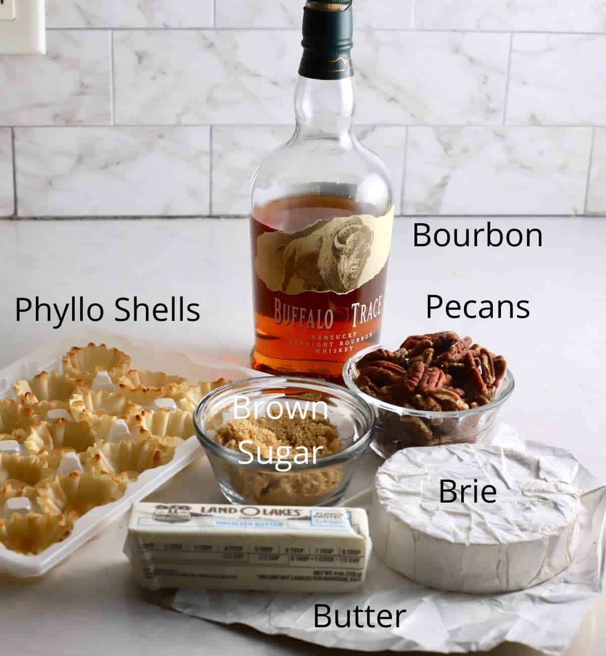 Ingredients to make brie bites including bourbon, phyllo shells, and brie cheese. 