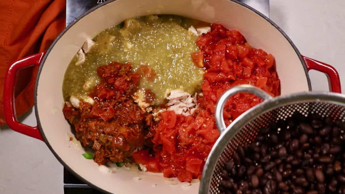 Diced tomatoes, salsa verde, black beans and other ingredients for chili in a Dutch oven.