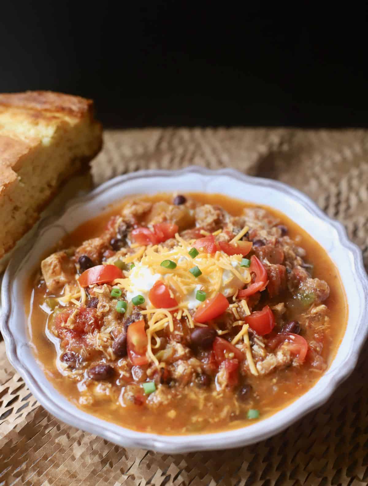 A bowl of salsa verde chicken chili with a piece of cornbread. 