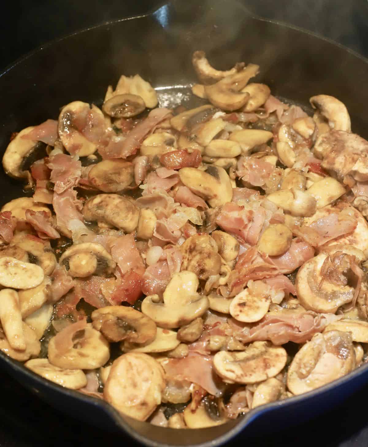 Cooking sliced mushrooms and prosciutto in a cast-iron skillet.