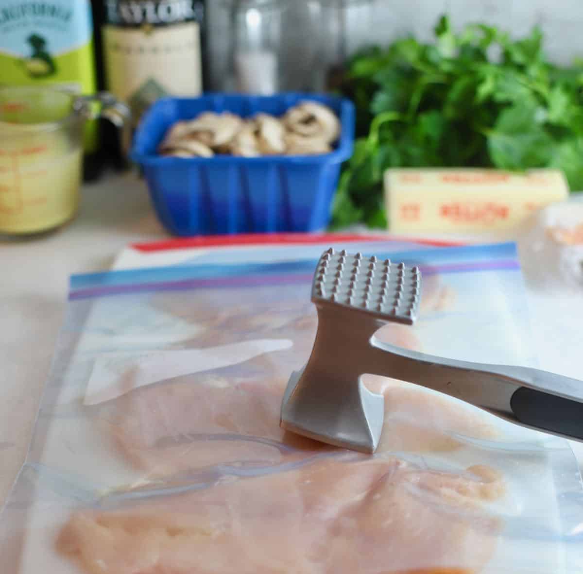 A meat mallet pounding chicken breasts to an even thickness.