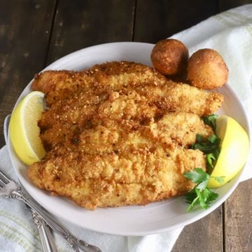 Fried fish fillets and hushpuppies on a white platter garnished with lemon slices.