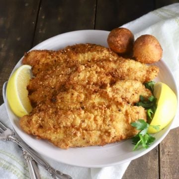 Fried catfish fillets on a white plate garnished with lemon slices.