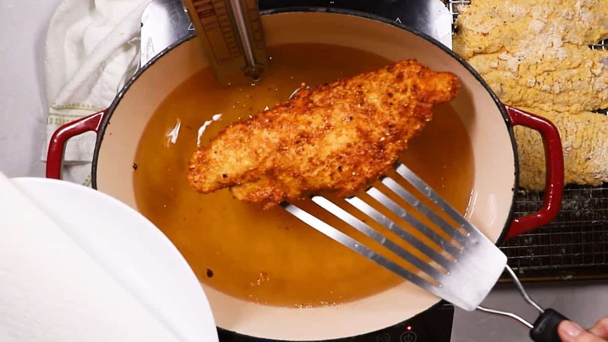 Using a fish spatula to remove a fried fish fillet from cooking oil. 