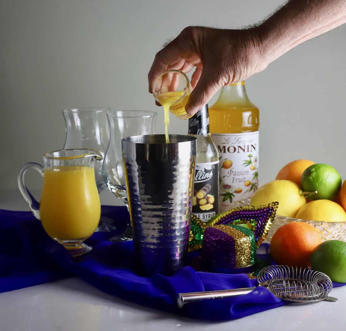 Adding a jigger of passion fruit juice to a metal cocktail shaker. 