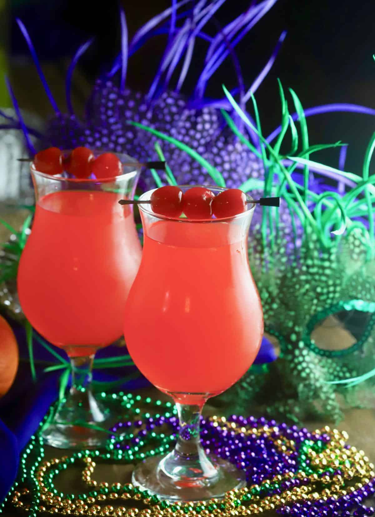 Two Hurricane cocktails on a table with Mardi Gras beads and masks. 