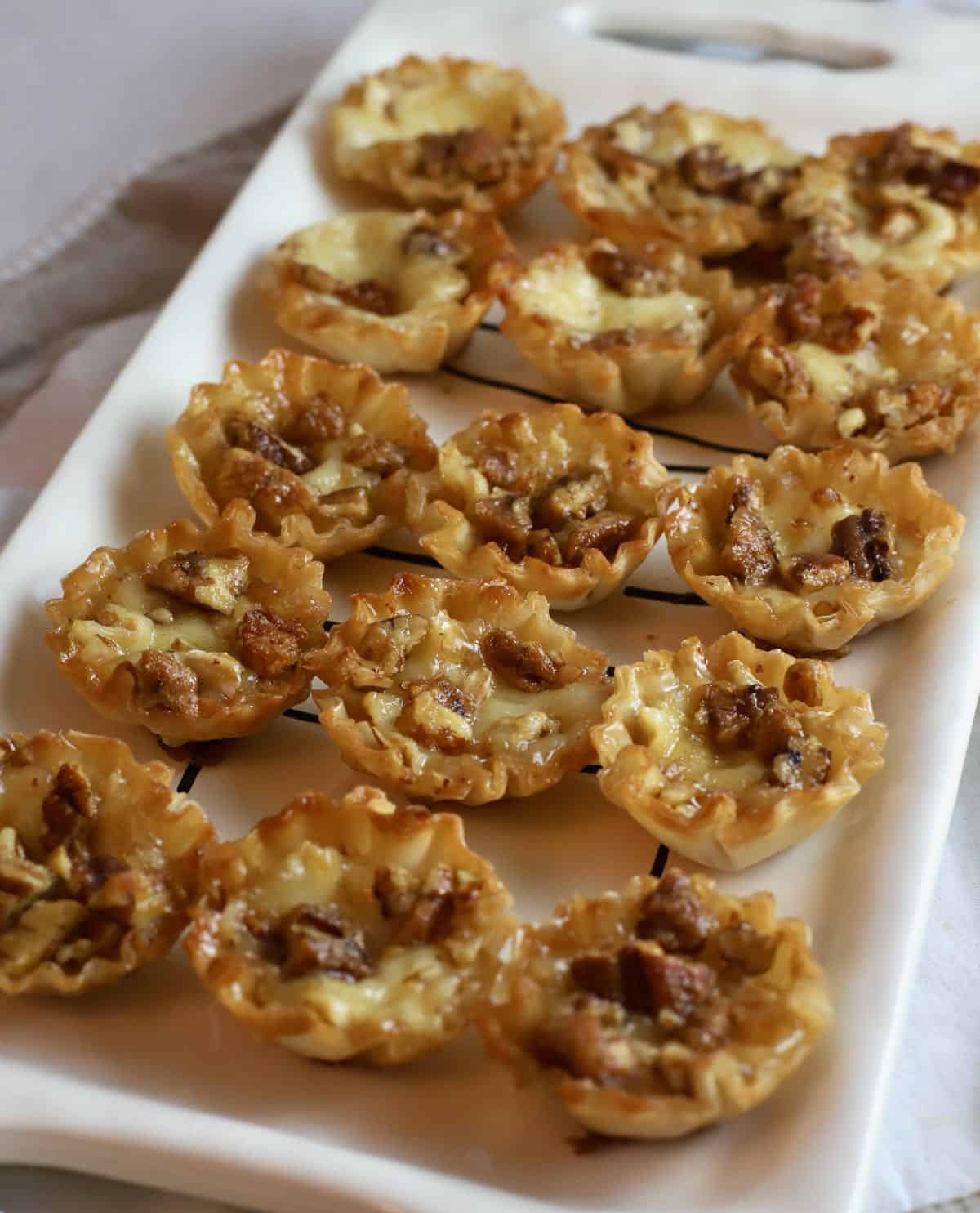 Bourbon pecan brie bites on a white serving tray. 