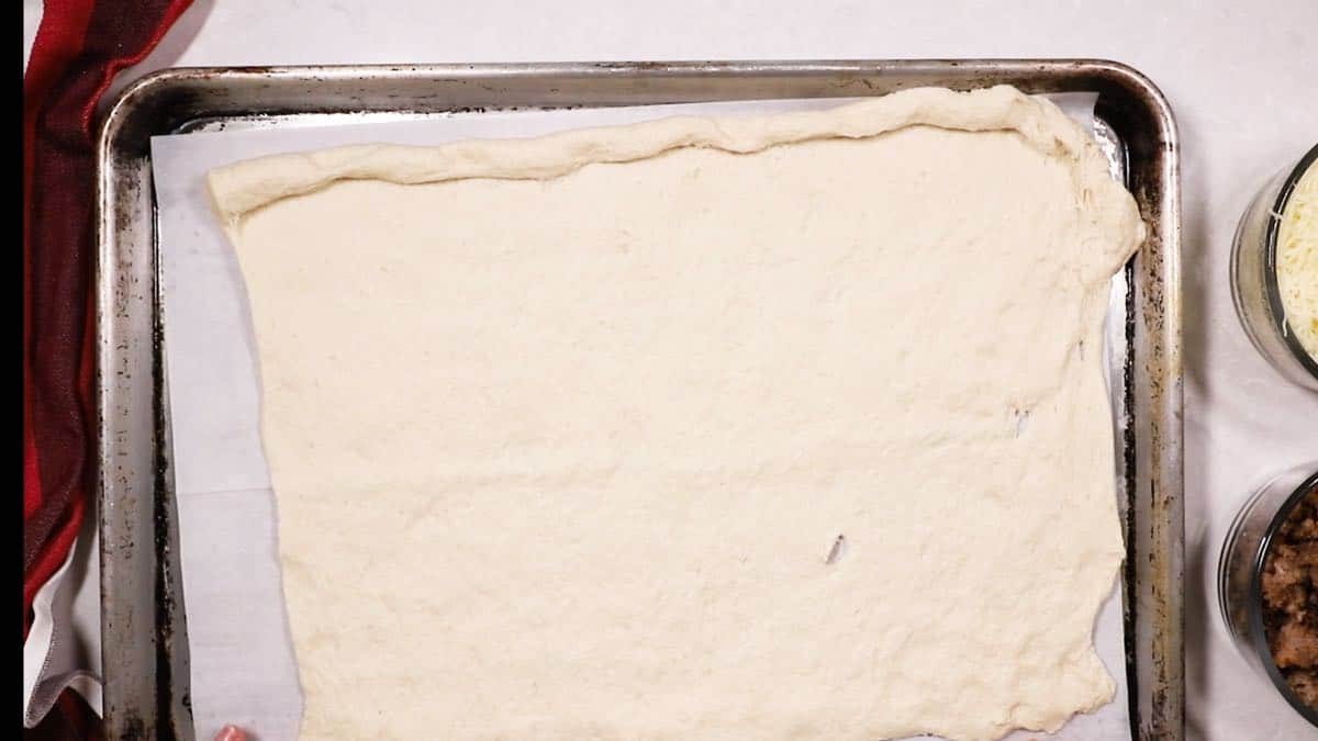 French bread dough spread out on a baking sheet. 
