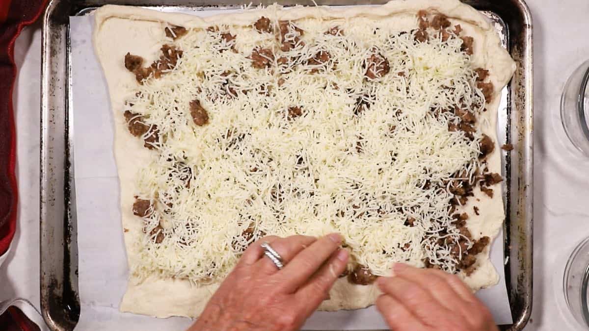 Shredded cheese covering sausage on bread dough. 