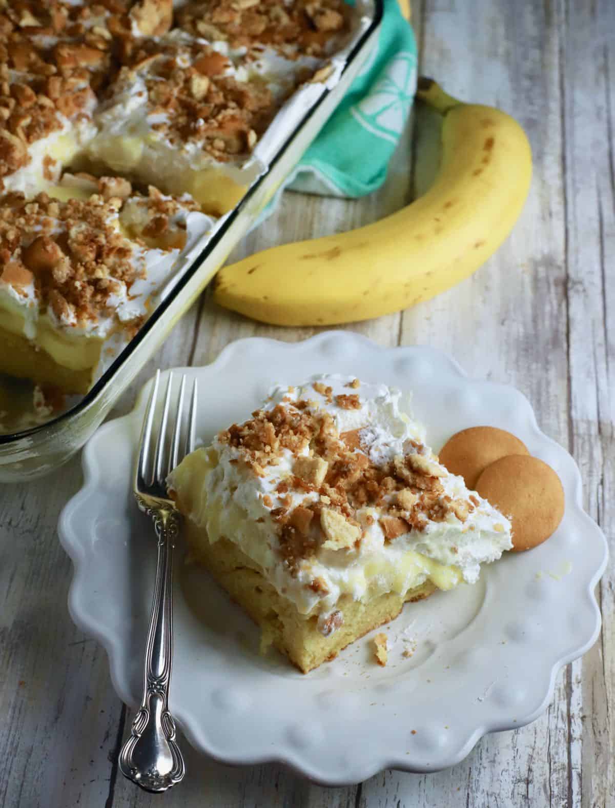 A square of banana pudding cake on a plate next to a banana. 