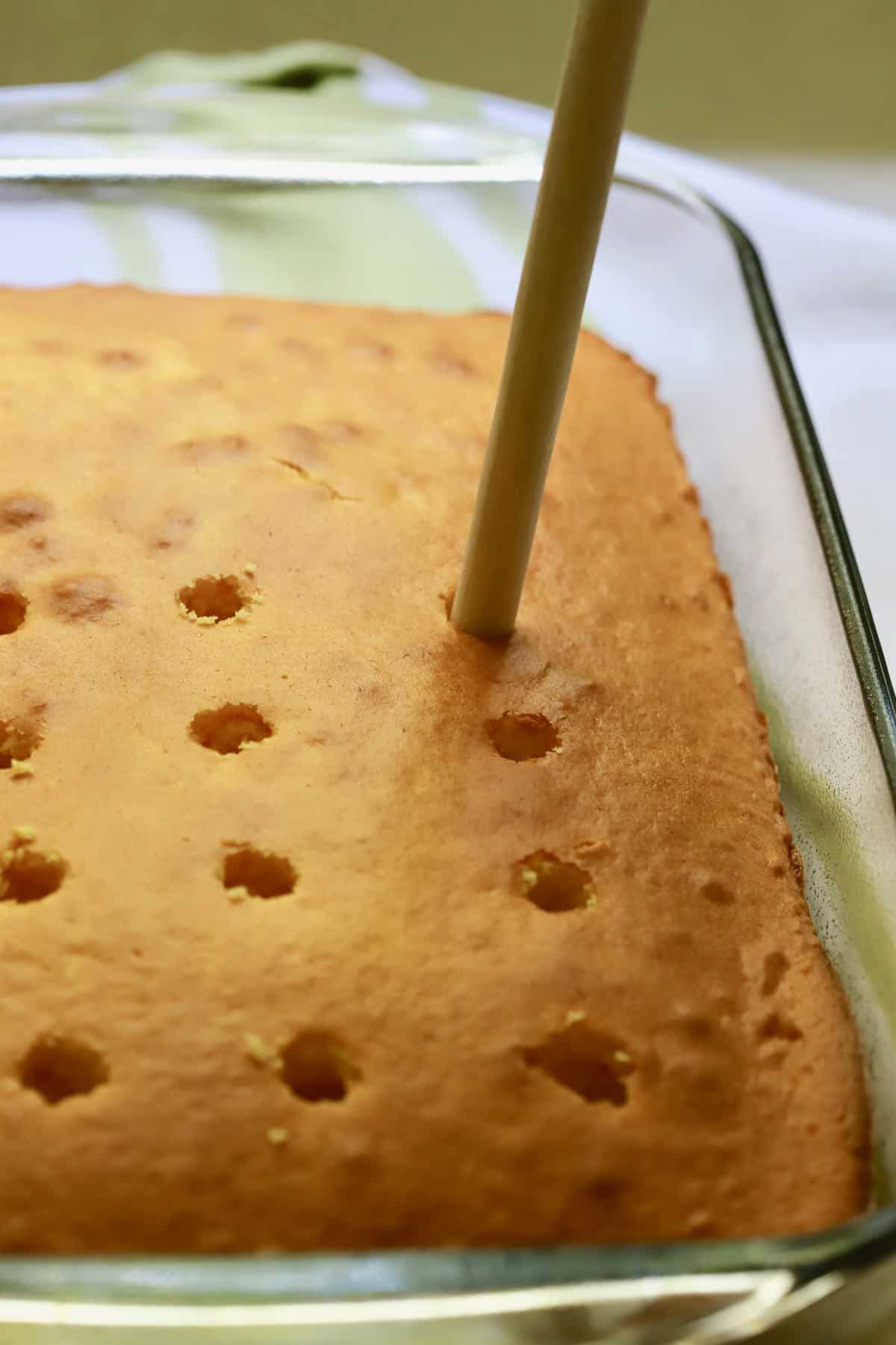 Poking holes into a sheet cake using a wooden spoon handle. 