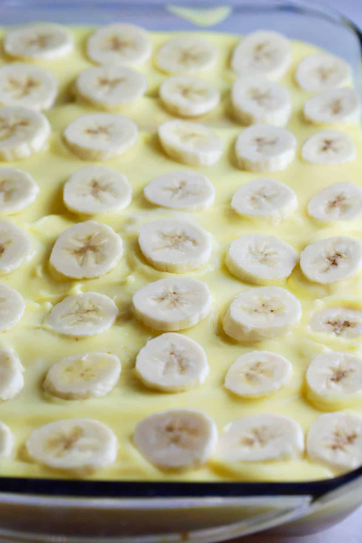 Sliced bananas cover a layer of pudding on a banana pudding cake. 