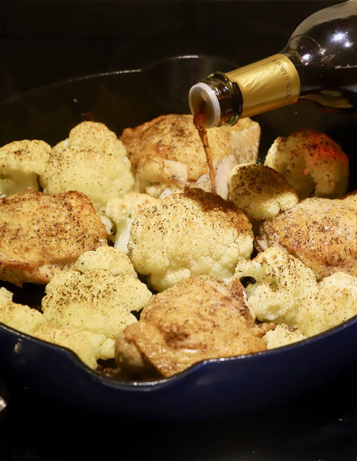 Pouring sherry vinegar in a cast iron skillet with chicken and cauliflower.