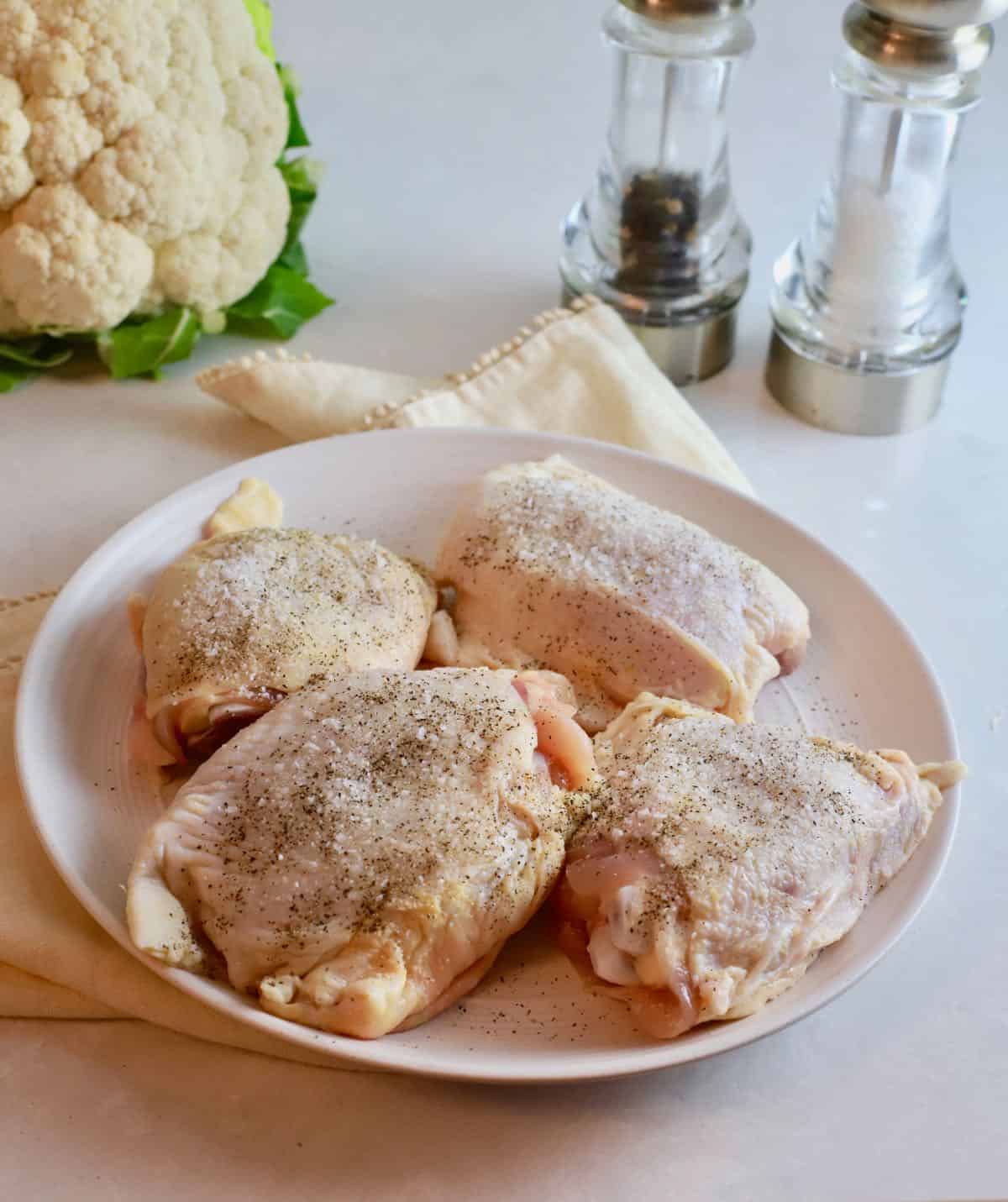 Four raw chicken thighs seasoned with salt and pepper. 