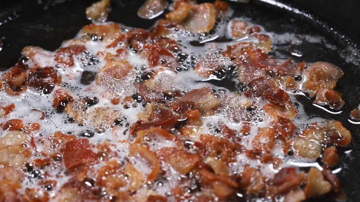 Bacon pieces cooking in a skillet.