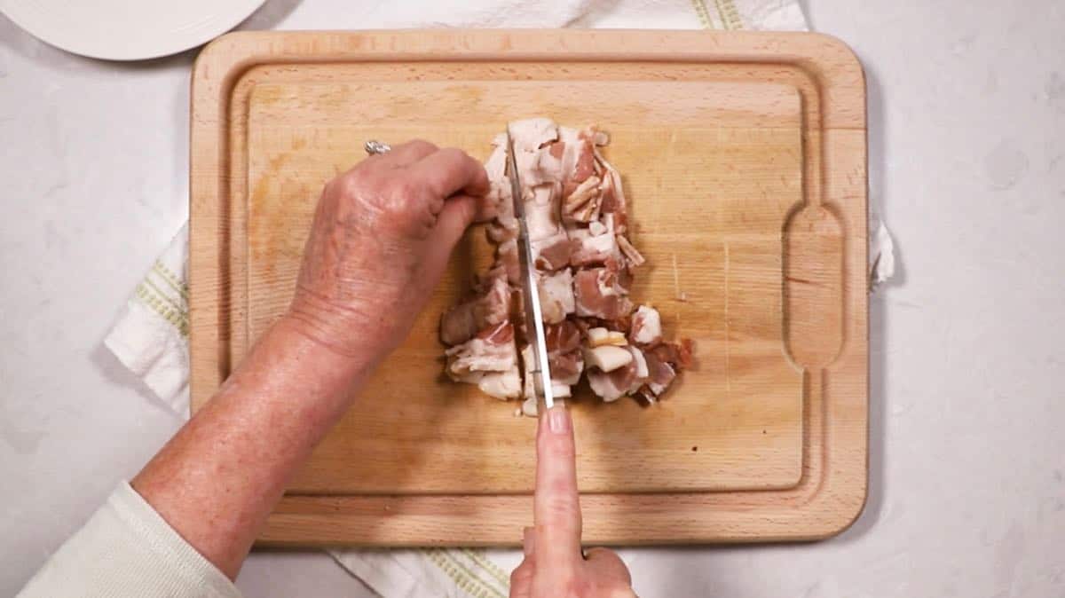 Cutting bacon with a knife on a cutting board.