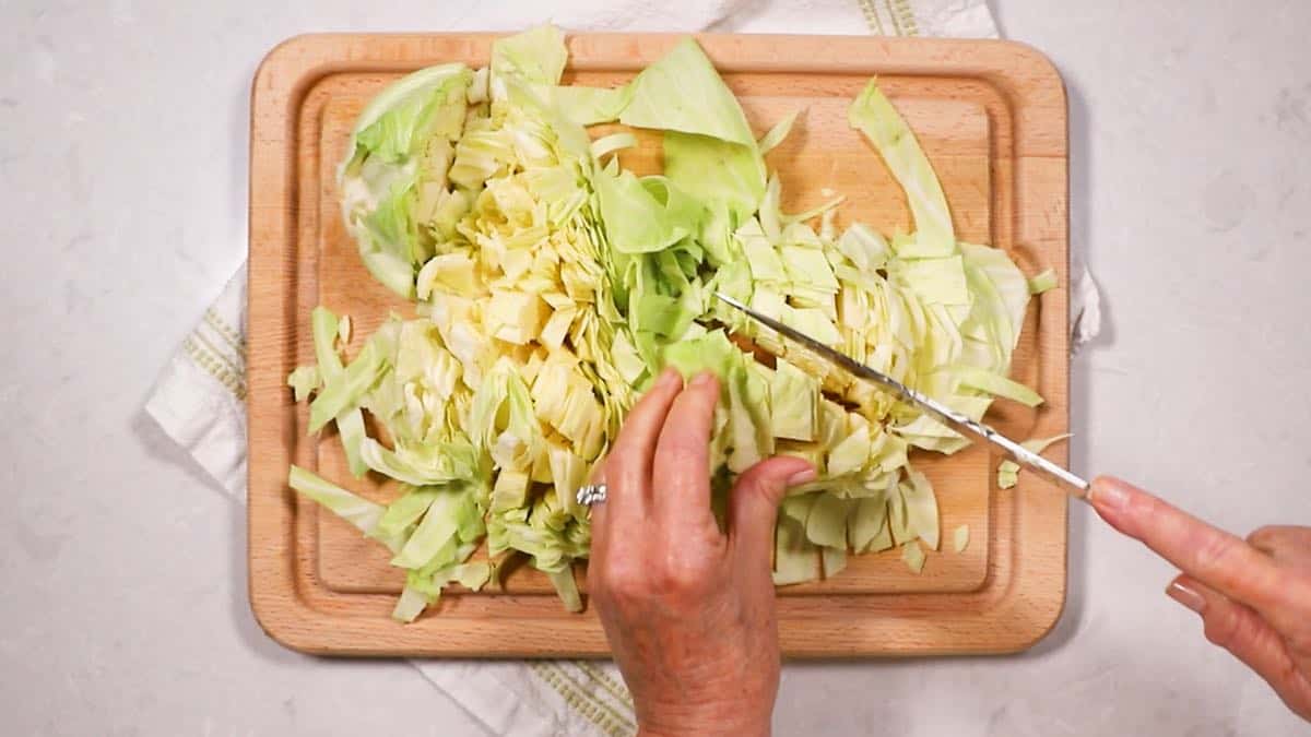 Cutting cabbage up with a knife on a cutting board.