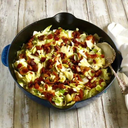 A cast iron skillet with Southern fried cabbage topped with bacon.