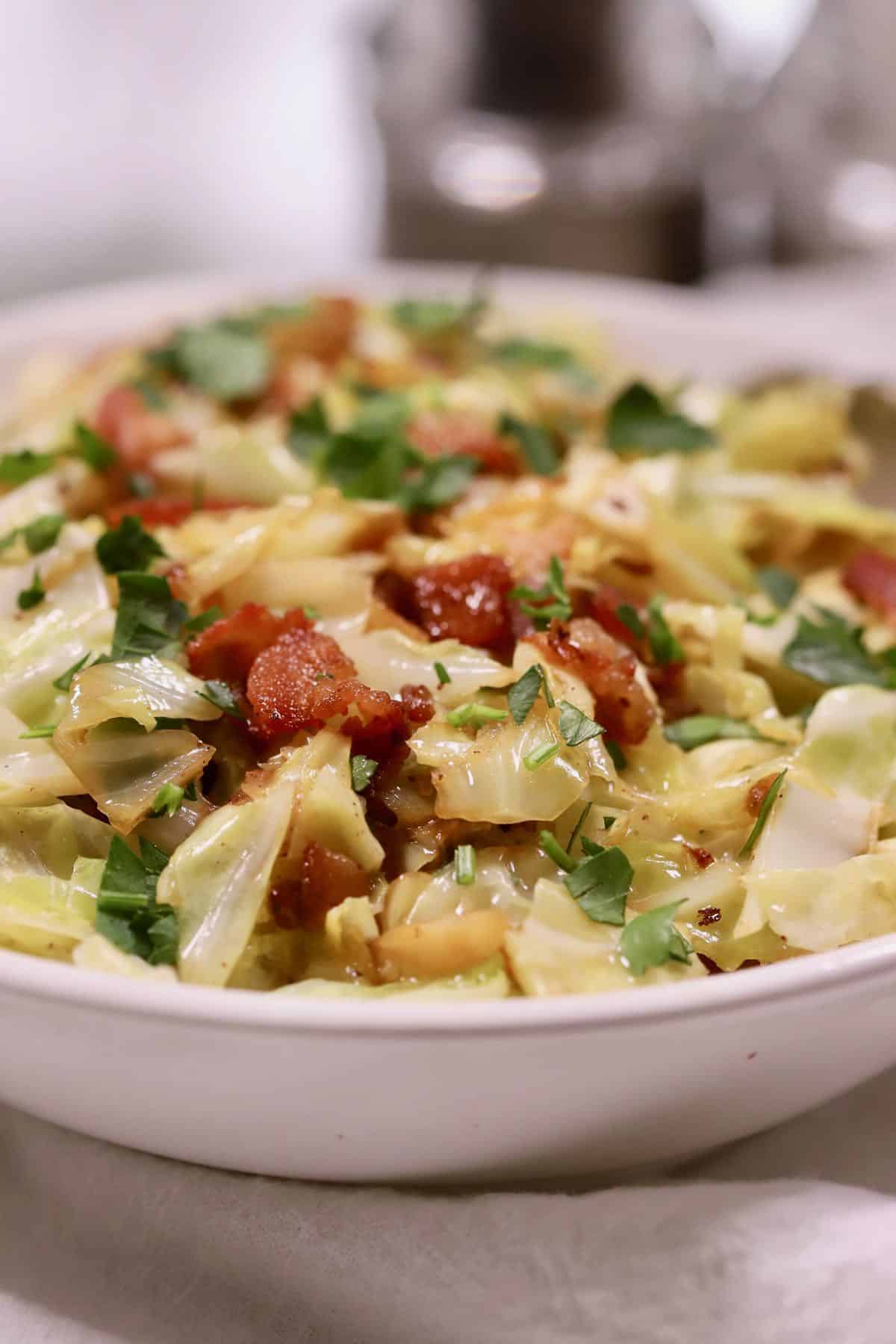 A large bowl full of fried cabbage topped with bacon. 