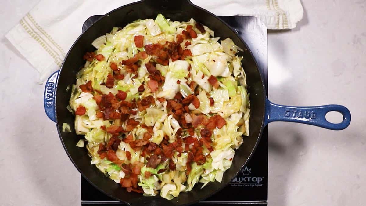 A cast iron skillet full of fried cabbage topped with bacon.