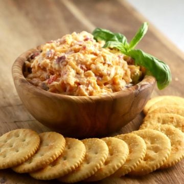 A bowl of pimento cheese spread in a bowl with crackers below it.