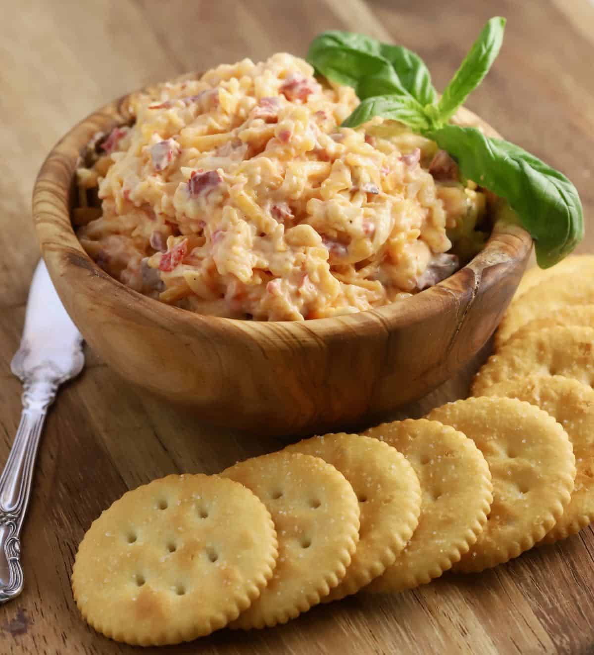 Pimento cheese in a small wooden bowl with a knife and crackers.