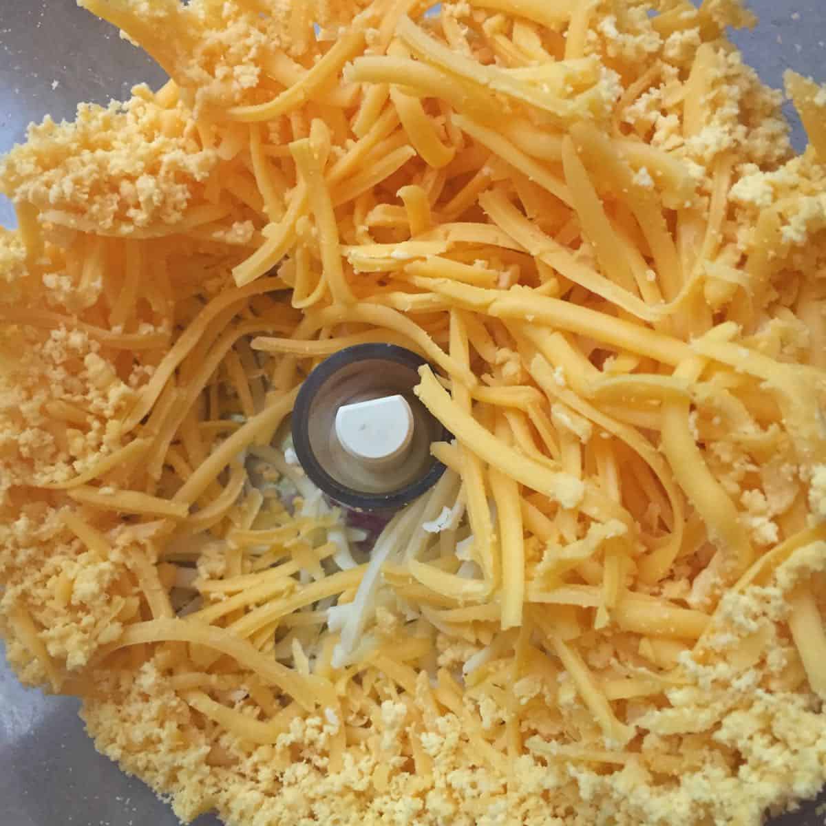 A food processor with grated cheese in the bowl. 