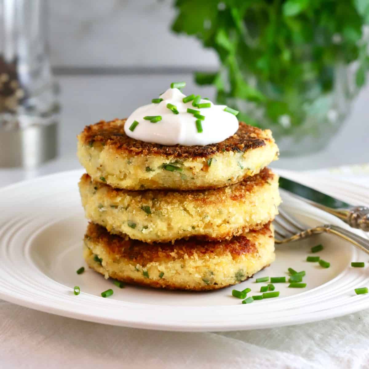 Three potato fritters topped with sour cream and chives on a plate.