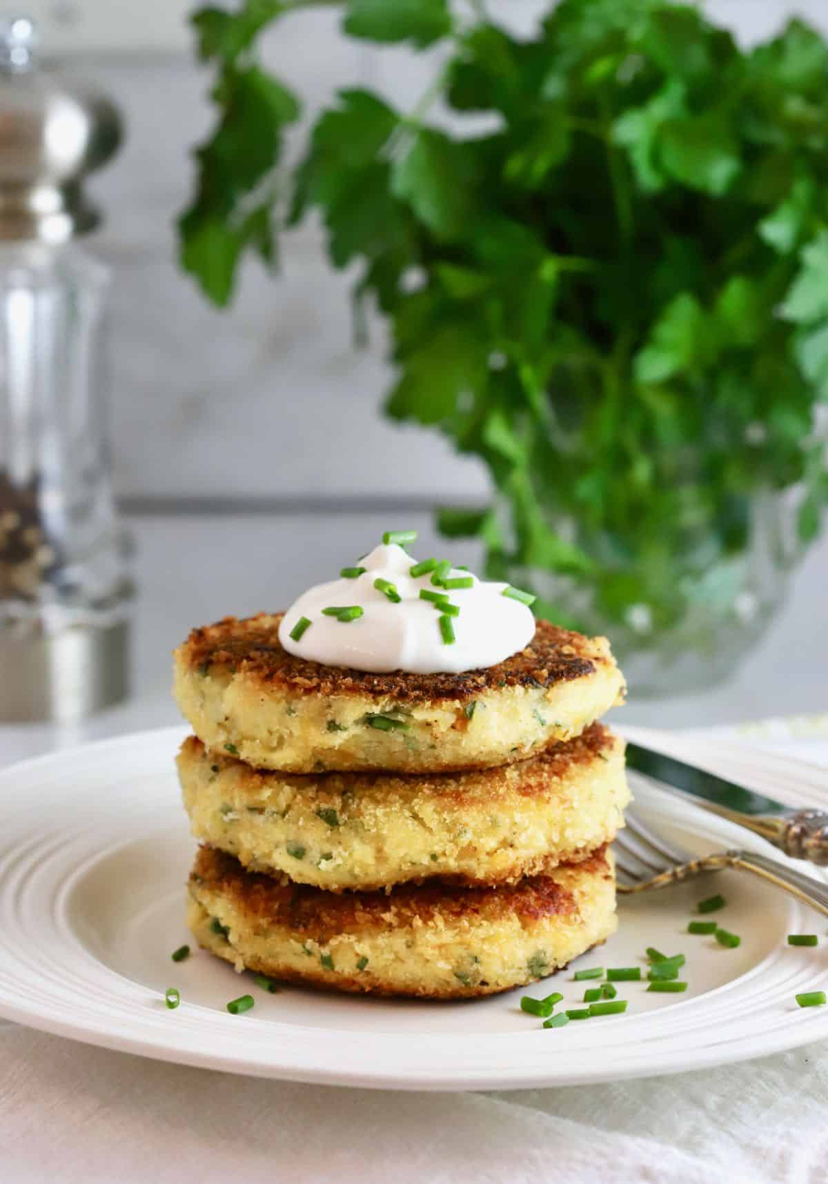Three potato fritters on a plate, topped with a dollop of sour cream. 