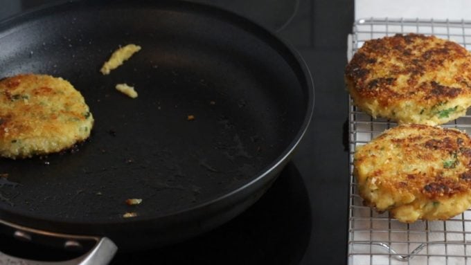 Removing potato fritters from a skillet and placing them on a wire rack.