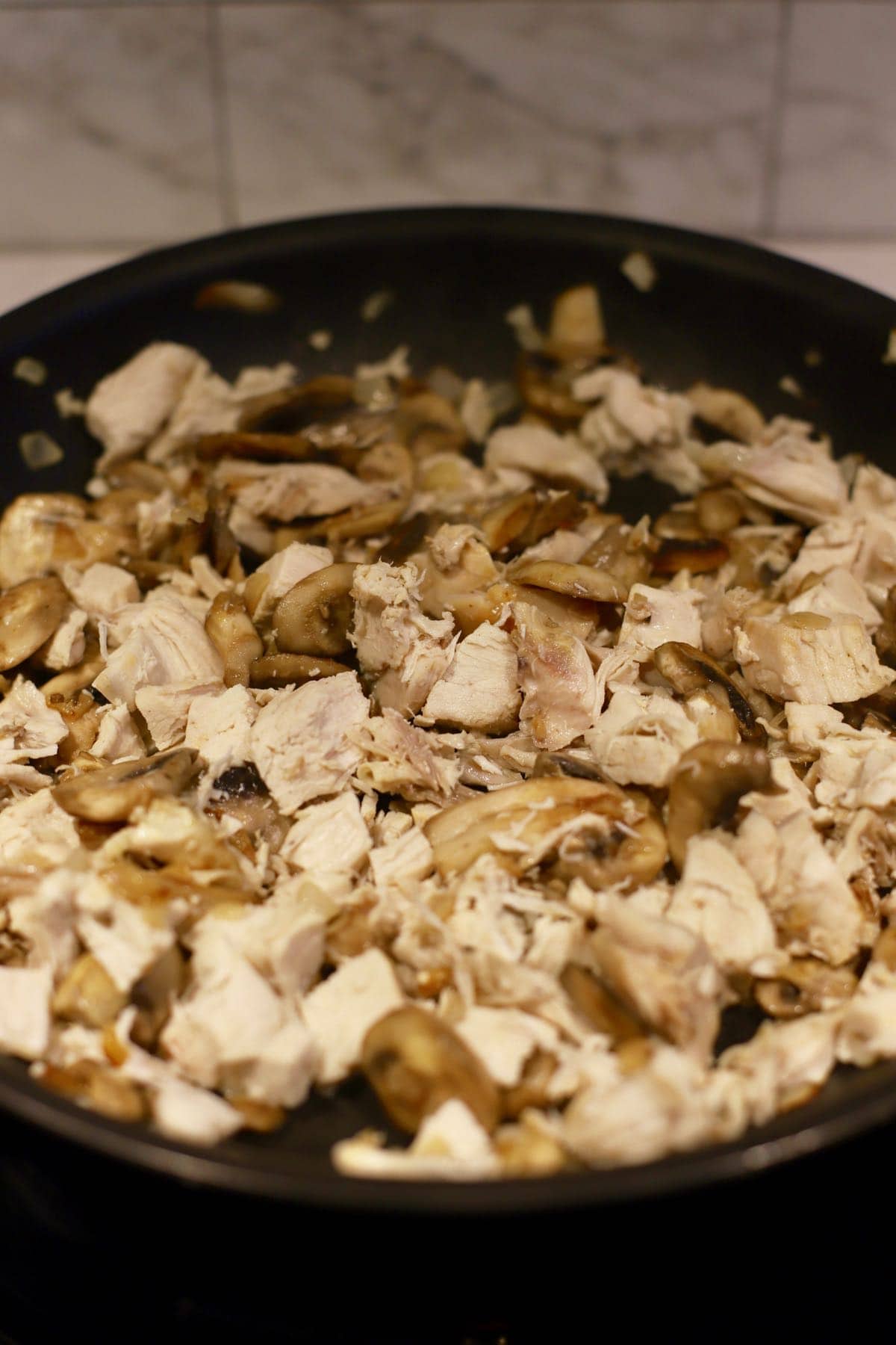 Pieces of cooked chicken and sliced mushrooms in a skillet.