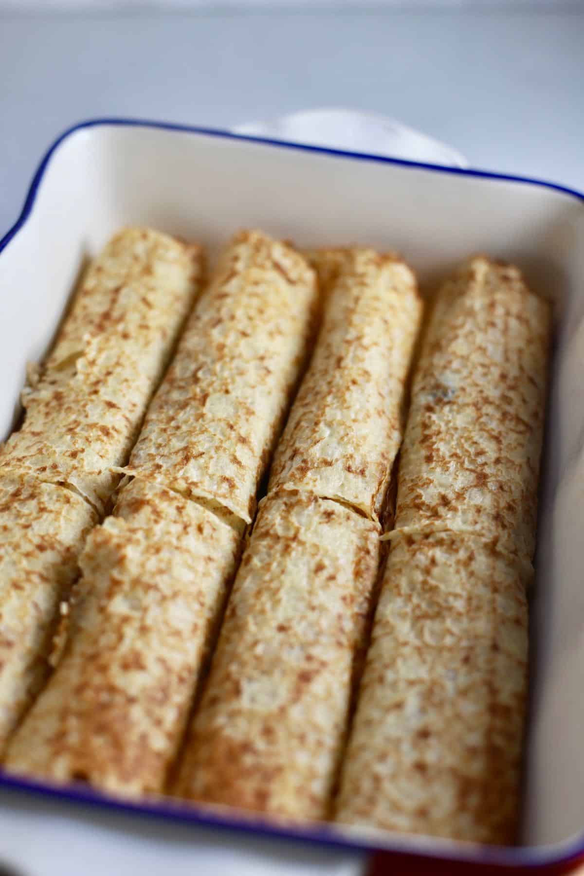 Unbaked crepes filled with chicken and mushrooms in a baking dish.