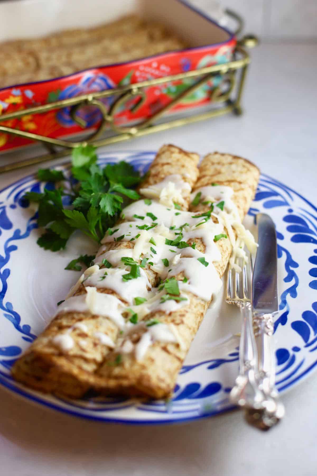 Chicken crepes on a blue and white dish with a knife and fork.