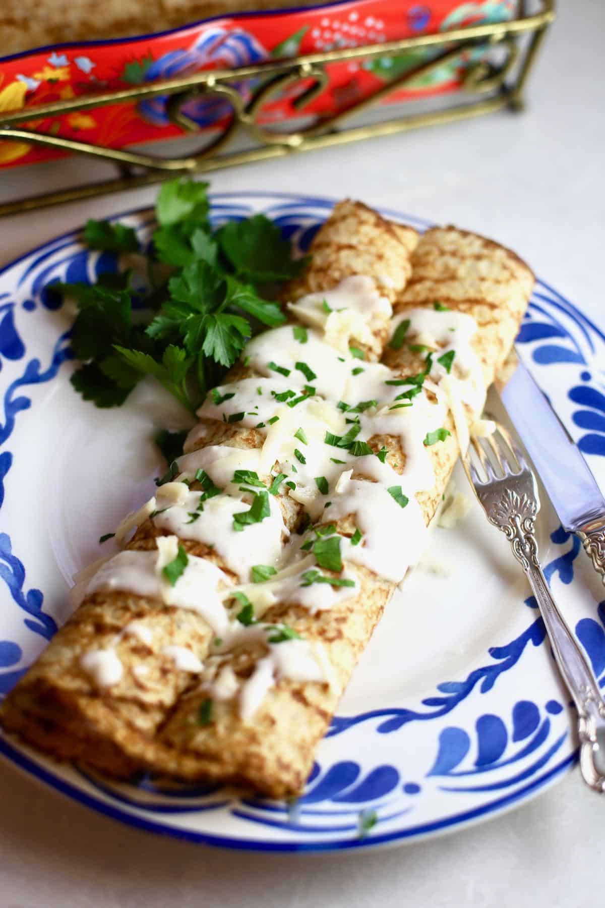 Two chicken crepes with mushrooms on a blue and white plate. 