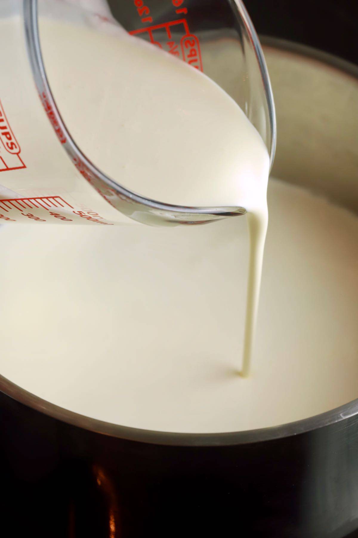 Pouring heavy cream into a saucepan.