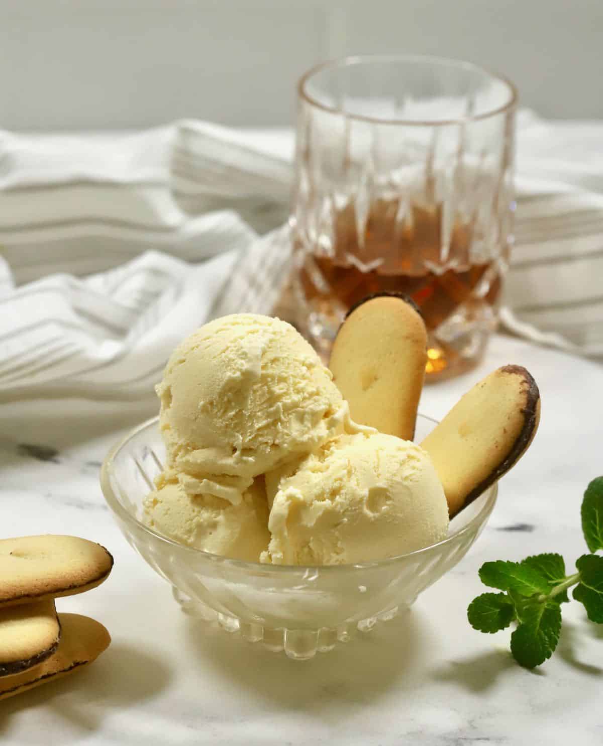 Bourbon ice cream in a bowl with cookies and a glass of bourbon in the back. 